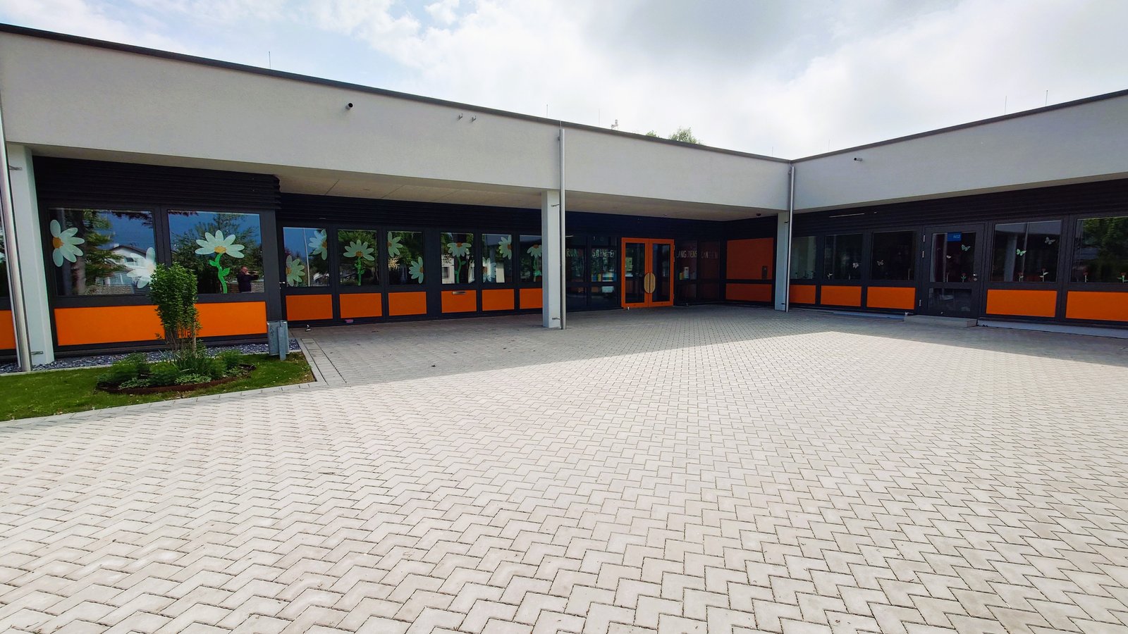 Eingang der frisch sanierten Grundschule Langenenslingen mit orange-grauer Fassade und gemalten Margeriten an den Fenstern